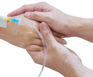 Man holding woman, patient, hand with a tube of medicine injection on a bed in a hospital